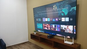 Un téléviseur à écran plat fixé au mur, avec une étagère en bois en dessous.