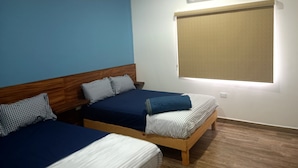 Une chambre avec deux lits simples, une tête de lit en bois, une fenêtre avec un store et un appareil de climatisation fixé au mur.