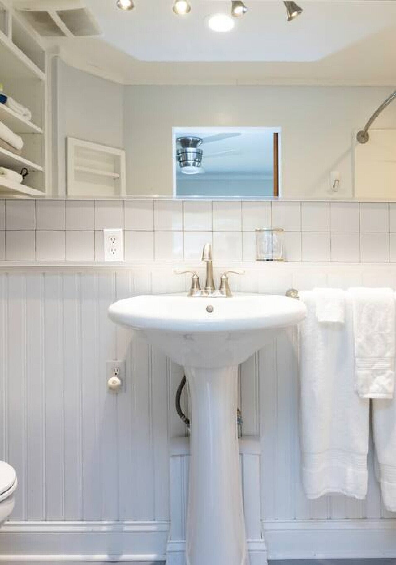 A bathroom with a pedestal sink, white tiles, and a towel rack.