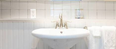 A bathroom with a pedestal sink, white tiles, and a towel rack.