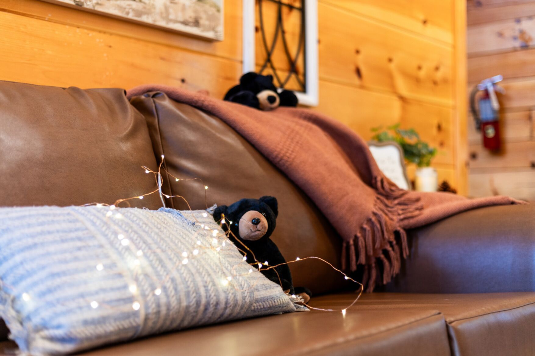 A cozy room with a brown leather sofa, a knitted pillow, and a teddy bear.