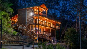 Una cabaña de madera de varios niveles con iluminación exterior, rodeada de árboles.