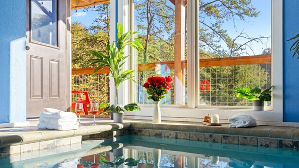 Zona de piscina con vistas despejadas del paisaje circundante, una terraza de madera y un ventanal con árboles a la vista.