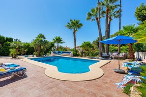 A swimming pool with a curved edge, surrounded by palm trees and a patio area with lounge chairs and umbrellas.