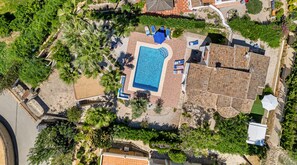 An aerial view of a property with a swimming pool surrounded by greenery, a tiled roof, and a paved area with lounge chairs. - Villa La Tranquilidad - Plus (Benissa)