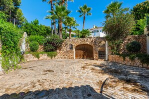 A stone courtyard with a wooden gate, surrounded by lush greenery and palm trees.