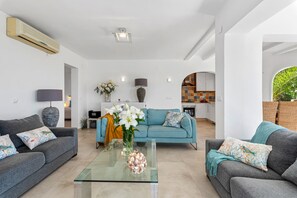A modern living room with two sofas, a glass coffee table, and a kitchen in the background.