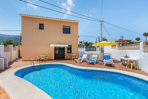 A swimming pool with lounge chairs and umbrellas, a building with a door and windows, and a clear sky. - Villa Caseta de Sau - PlusHolidays (Calpe)