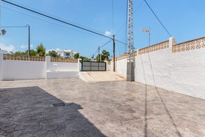 A paved courtyard with a white wall and a gate, surrounded by power lines and a street lamp.