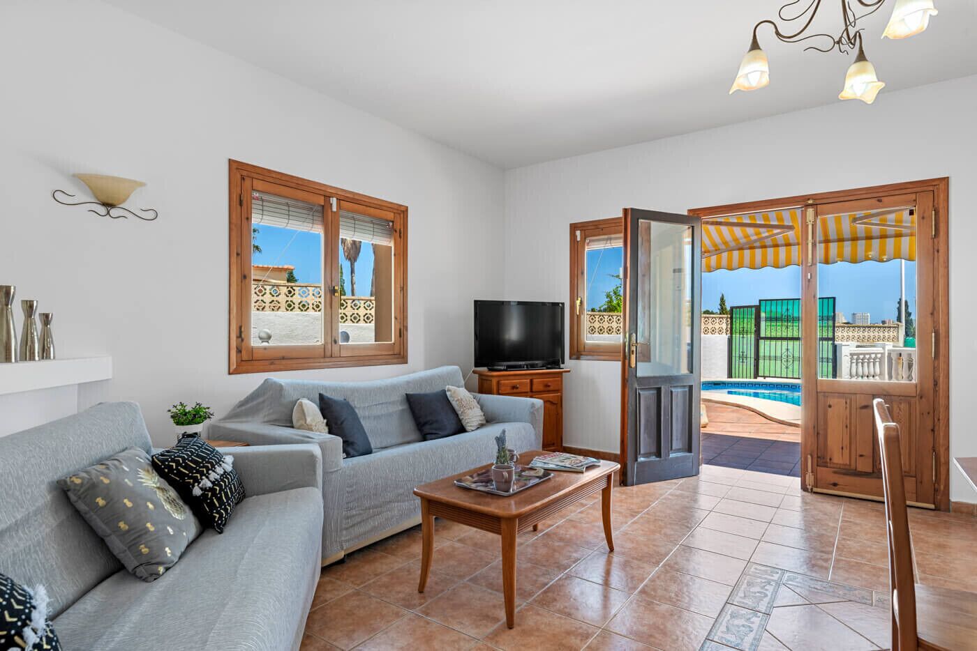 A living room with a sofa, TV, and a view of a pool through a door.