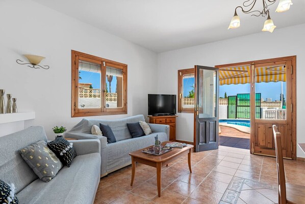 A living room with a sofa, TV, and a view of a pool through a door.