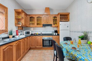 A kitchen with wooden cabinets, a microwave, an oven, a refrigerator, and a dining table with a patterned tablecloth.