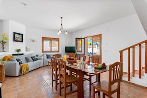 A spacious living area with a dining table set for four, a sofa, a television, and a view of the outside. - Villa Caseta de Sau - PlusHolidays (Calpe)