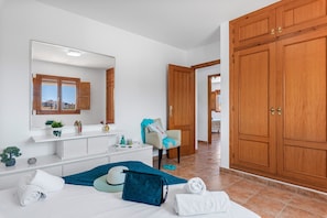 A hotel room with a large wooden wardrobe, a white vanity with a mirror, a bed with blue and white linens, and a small potted plant.
