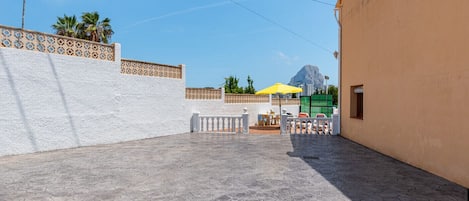 A courtyard with a tiled floor, a white wall with a decorative pattern, and a yellow umbrella.