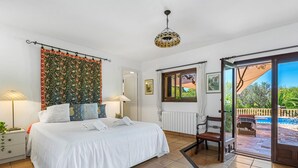 Ein Schlafzimmer mit einem Bett, zwei Nachttischlampen, einem Fenster mit Blick und einer Tür zu einem Außenbereich.