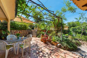 Una terrazza esterna con tavolo e sedie, circondata da piante in vaso e un muro in pietra.