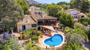 Eine Villa im mediterranen Stil mit Swimmingpool, umgeben von üppiger Vegetation und einer Bergkulisse.