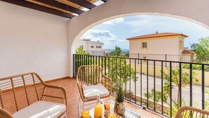 Un balcón con mobiliario de mimbre, una mesa con bebidas y vistas a un edificio de enfrente.