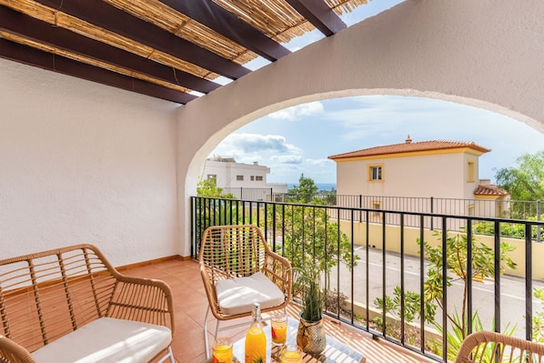 Un balcone con mobili in vimini, un tavolo con bevande e vista su un edificio di fronte.