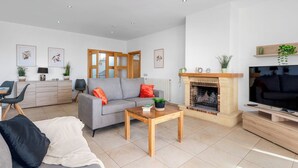 A modern living room with a grey sofa, a coffee table, a fireplace, and a television. - Villa Esperanza - PlusHoliddays (Calpe)