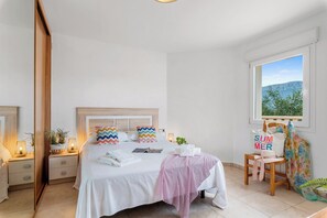 A bedroom with a bed, bedside tables, a window with a view, and a chair with a floral chair cover.
