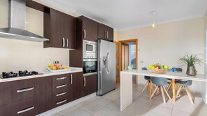 A modern kitchen with dark wooden cabinets, stainless steel appliances, and a white countertop. - Villa Esperanza - PlusHoliddays (Calpe)