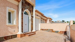 A building with a paved entrance, a white door, and a stone facade. - Villa Esperanza - PlusHoliddays (Calpe)