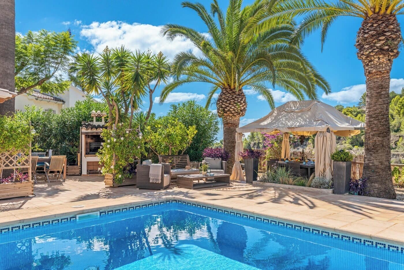 A pool area with a hot tub, lounge chairs, and a pergola with a canopy.