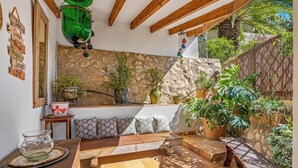 A cozy outdoor seating area with a stone wall backdrop, wooden beams, and various potted plants.