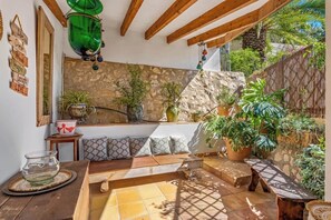 A cozy outdoor seating area with a stone wall backdrop, wooden beams, and various potted plants.