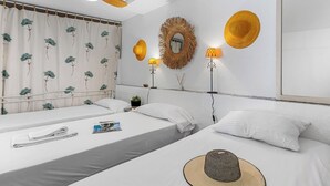 A hotel room with two beds, a ceiling fan, a mirror, and wall-mounted lamps.