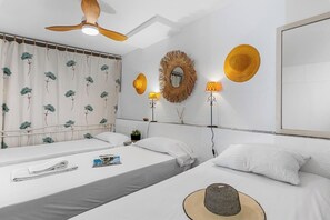 A hotel room with two beds, a ceiling fan, a mirror, and wall-mounted lamps.