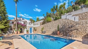A swimming pool with a stone wall and palm trees in the background. - Villa Domingo - PlusHolidays (Benissa)