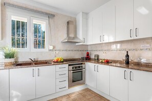 A modern kitchen with white cabinets, a stainless steel oven, a coffee maker, and a window with decorative iron bars.