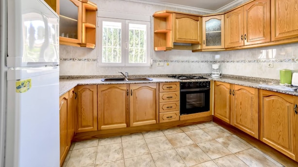Une cuisine avec des meubles de rangement en bois, un four encastré, un évier et une fenêtre donnant sur un paysage verdoyant.