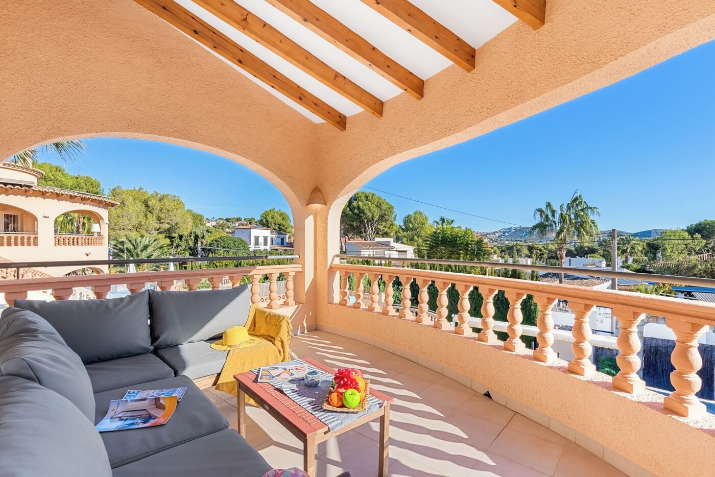 A balcony with a sofa, a table with fruits, and a view of a residential area.