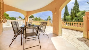 Un espace extérieur abrité, aménagé pour les repas, avec une table et des chaises, un sol carrelé et une vue sur le paysage environnant.