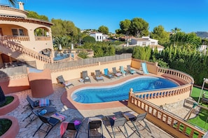 A pool area with lounge chairs and a hot tub, surrounded by a stone wall and a staircase.