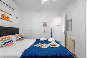 A hotel room with a bed, a blue knitted throw, a white hat, and a wall-mounted TV.