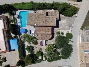 An aerial view of a property with a swimming pool, a covered patio area, and a variety of trees and shrubs.