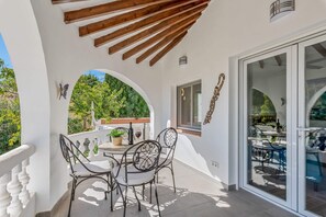 Eine Terrasse mit Tisch und Stühlen, einem Blumentopf und Blick auf den Garten durch eine Glastür.