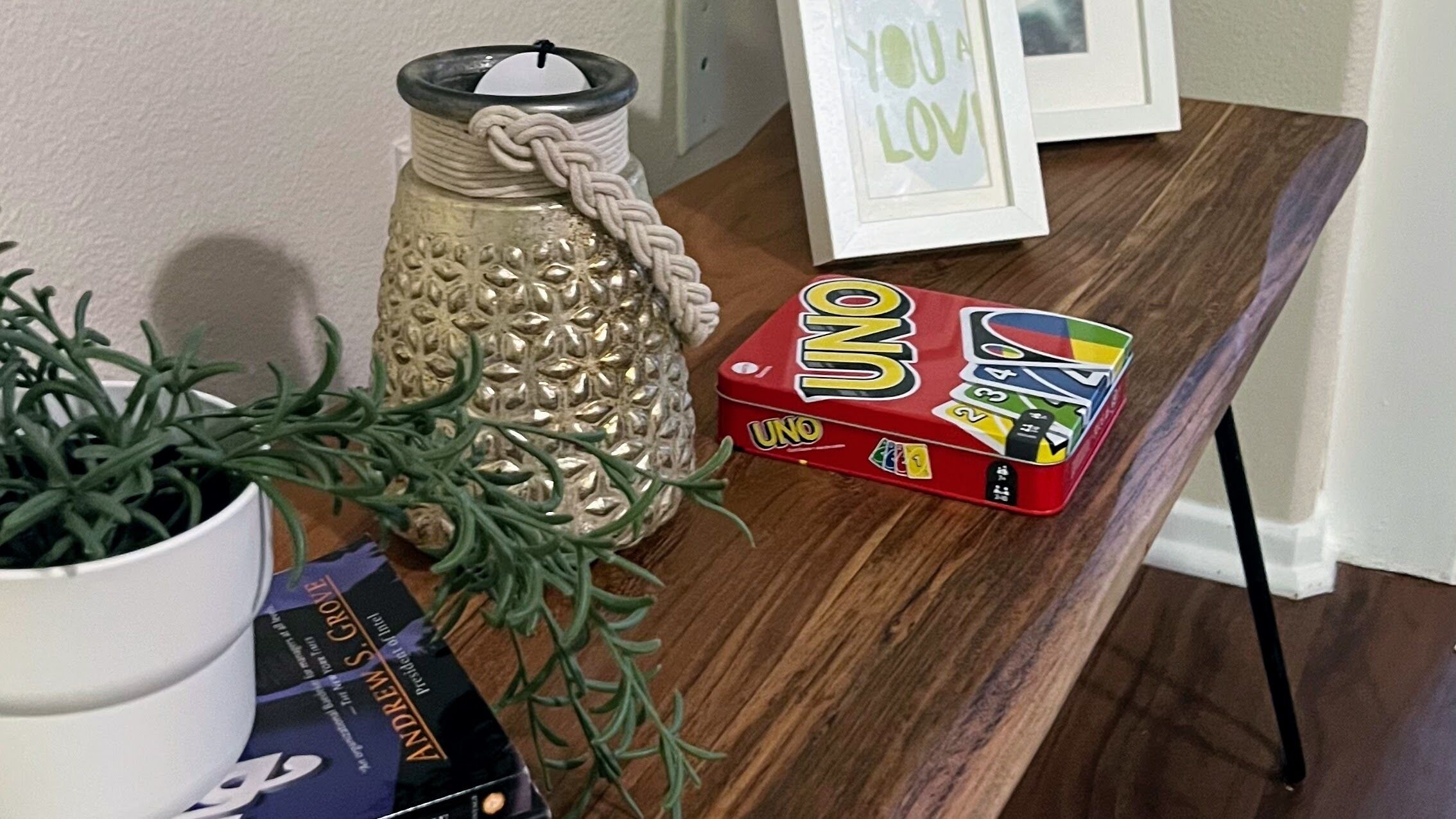 A wooden table with a UNO game box, a candle in a decorative jar, and a framed picture with the text "YOU A LOVE".
