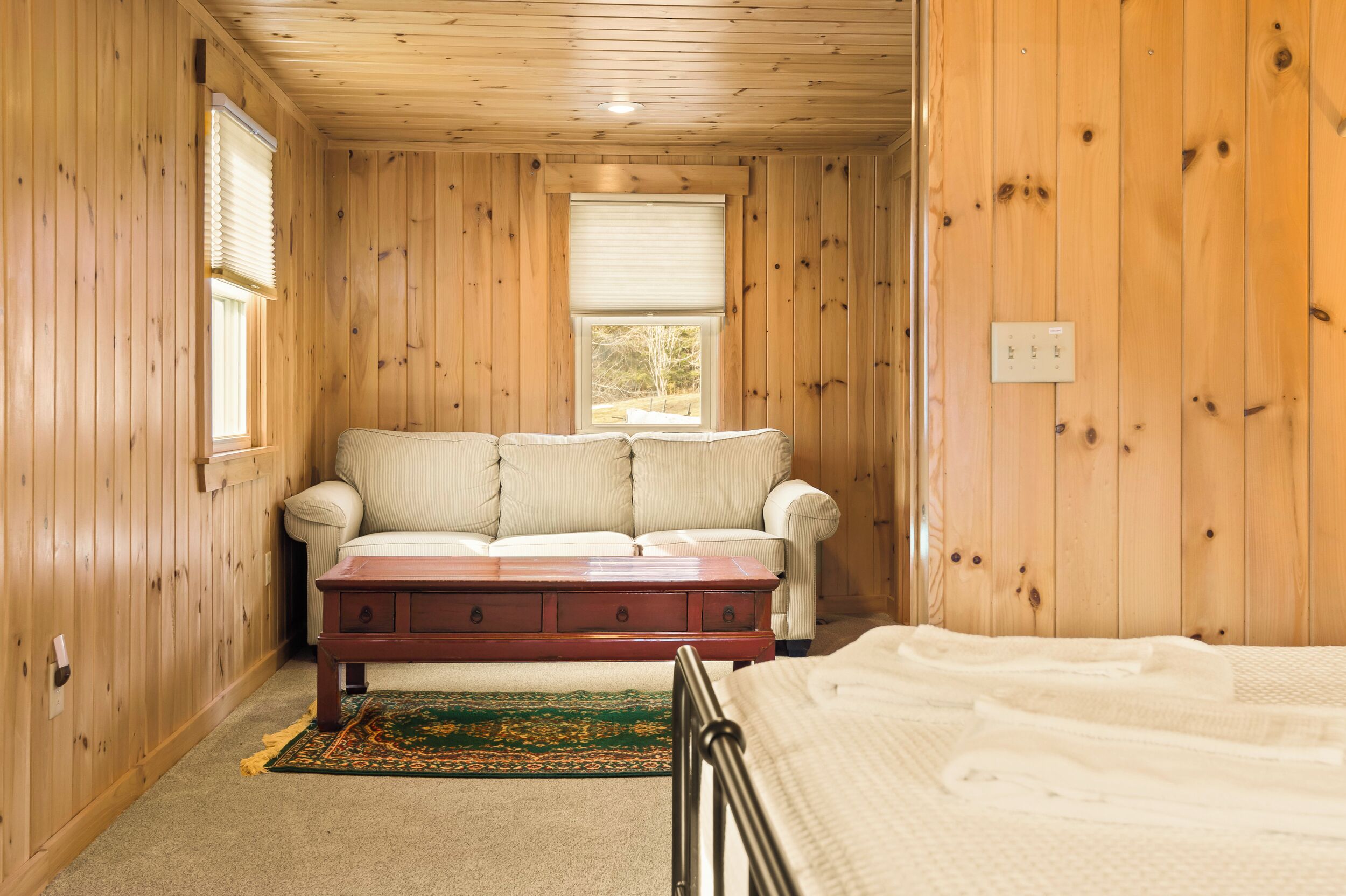 A cozy room with wooden walls, a white sofa, a wooden coffee table, and a bed.