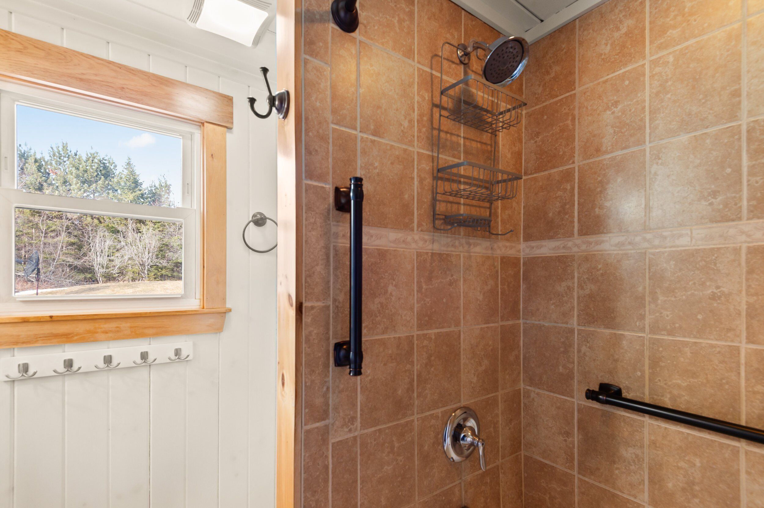 A bathroom with a shower, a window with a view of trees, and a towel rack.