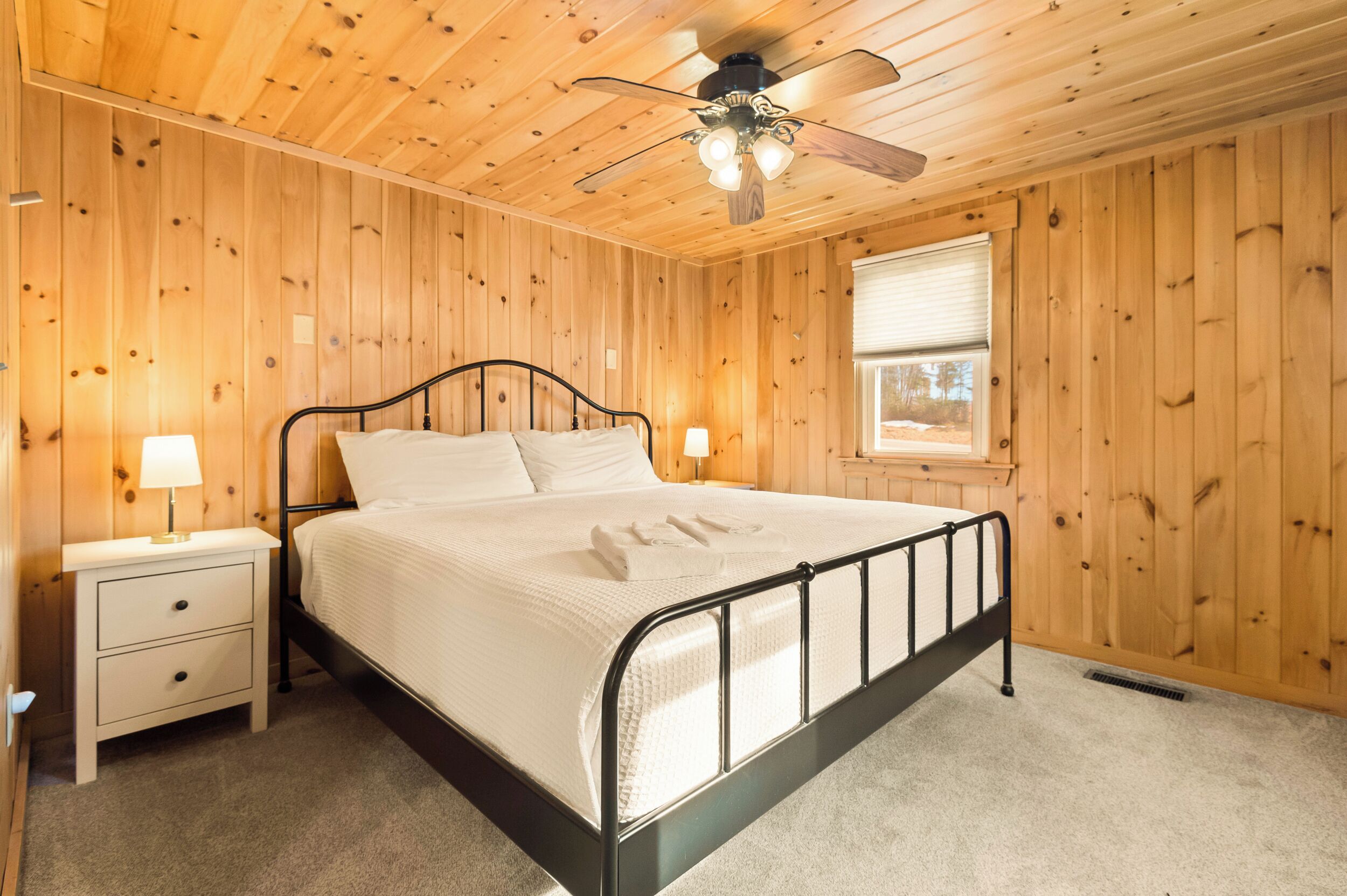 A wooden-paneled bedroom with a bed, two bedside tables, and a ceiling fan.