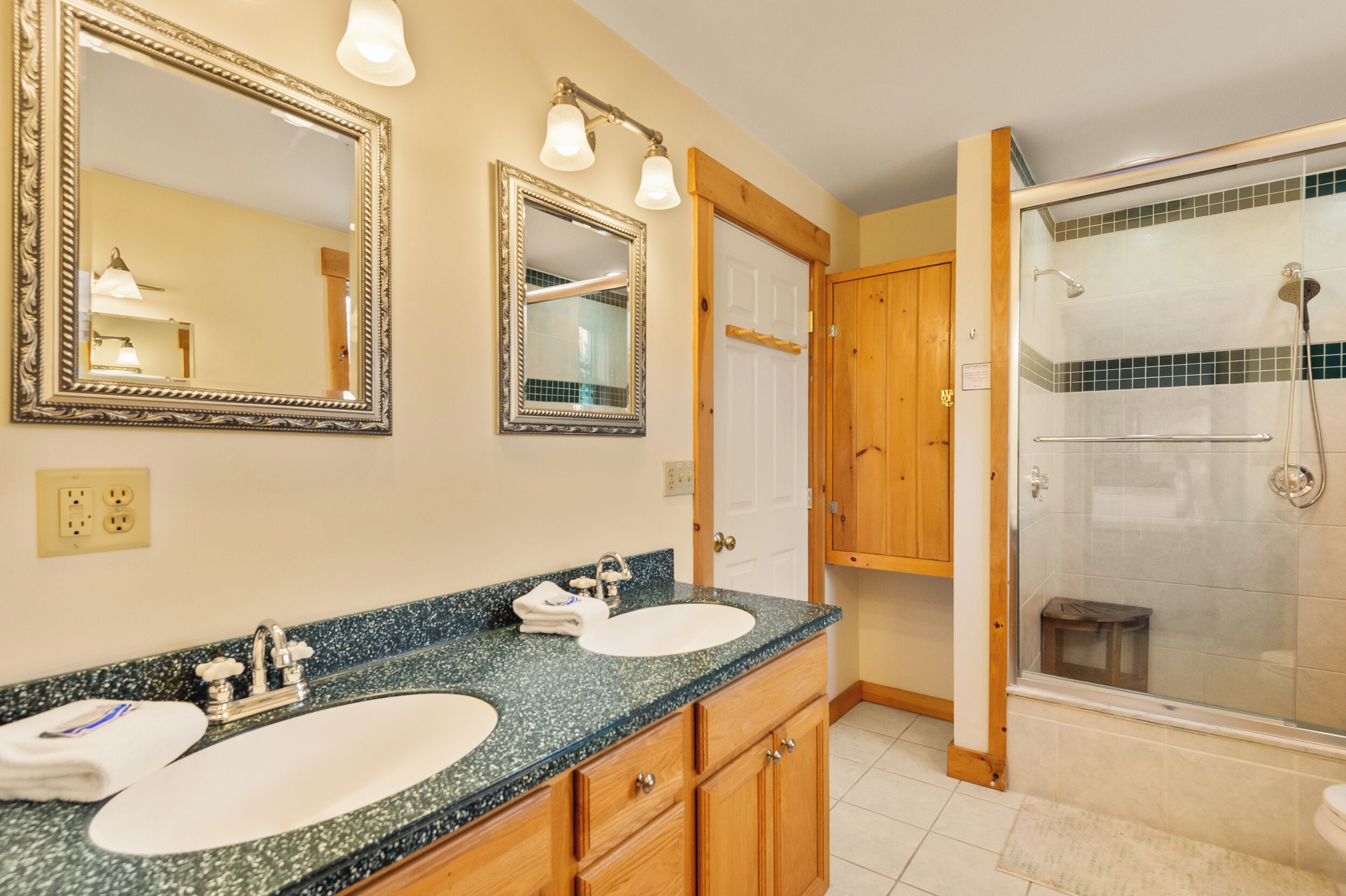 A bathroom with two sinks, wooden cabinets, a large mirror, and a glass-enclosed shower.