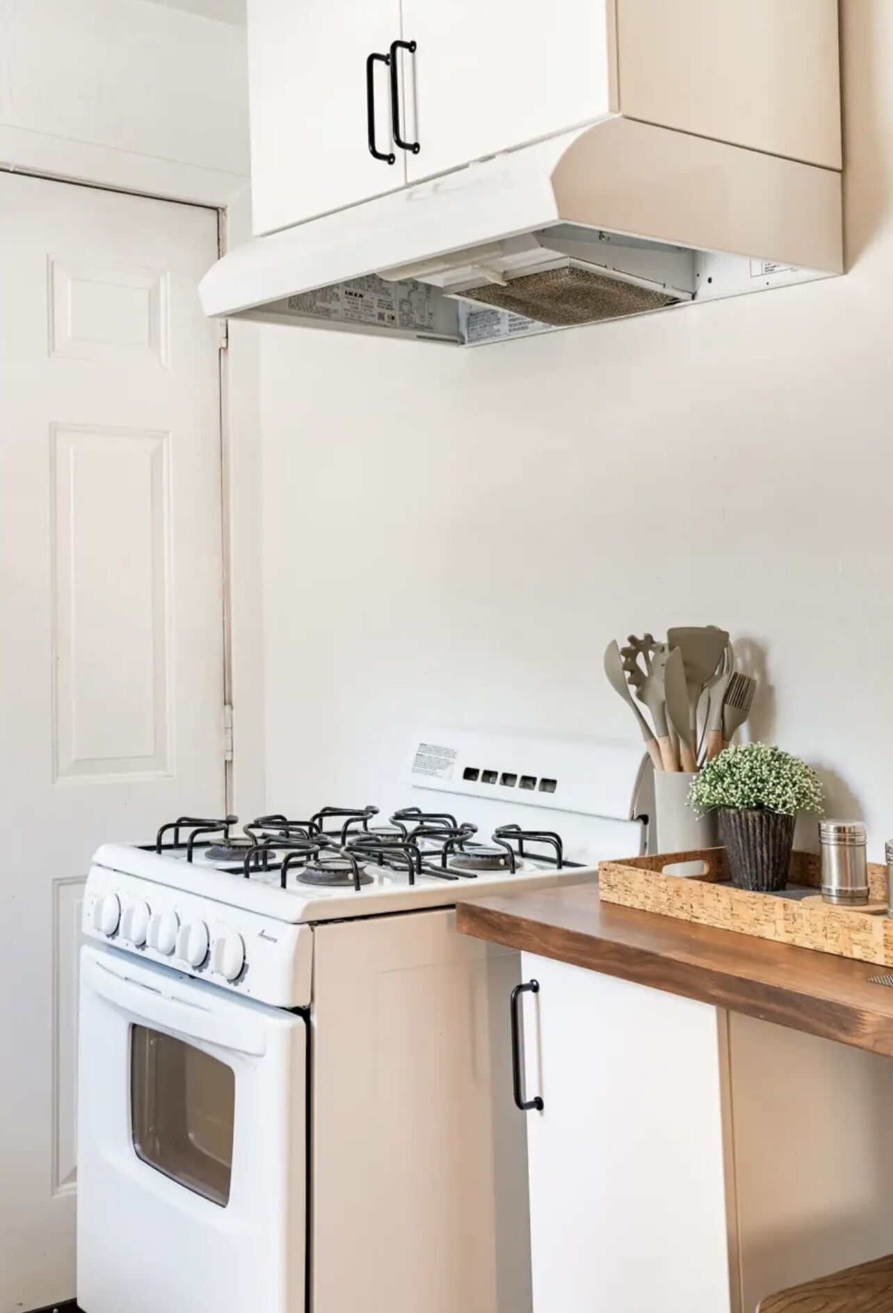 Una cucina con piano cottura bianco, mobili in legno e un ripiano con utensili da cucina e una piccola pianta.