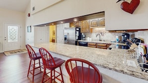 A kitchen with a large island, red bar stools, wooden cabinets, and a heart-shaped decoration on the wall.