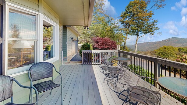 A wooden deck with outdoor furniture, a view of the surrounding landscape, and a mountain in the background.